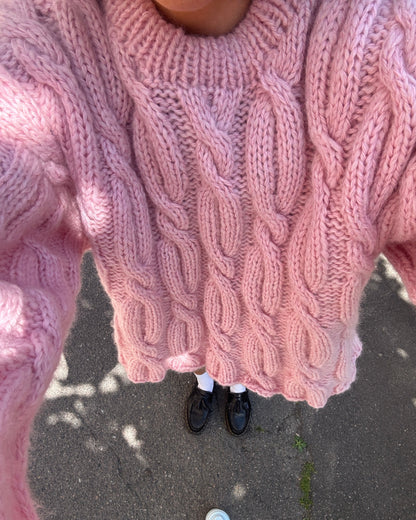 Person wearing a pink cable knit sweater on a concrete surface