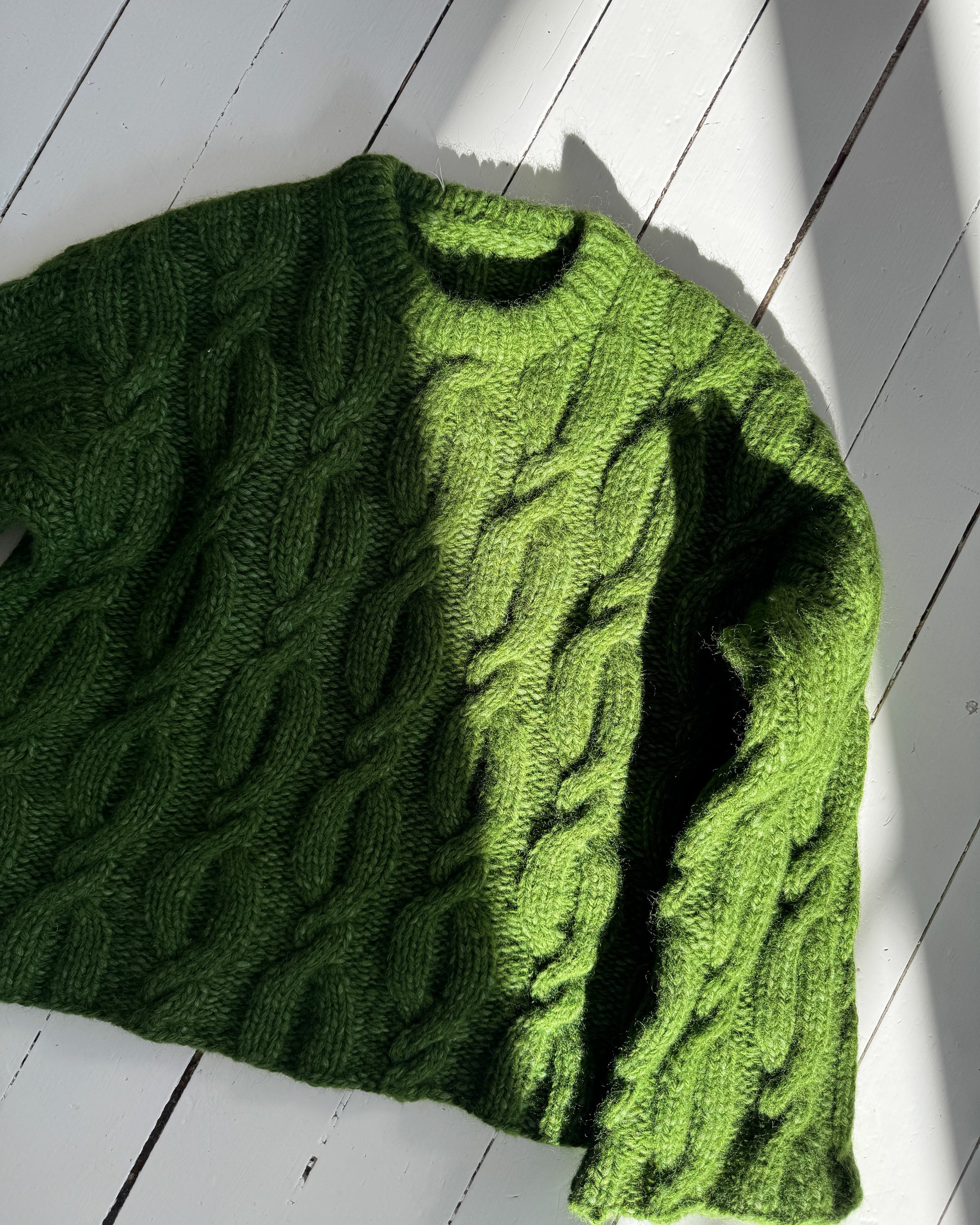Green knitted sweater on a white wooden floor
