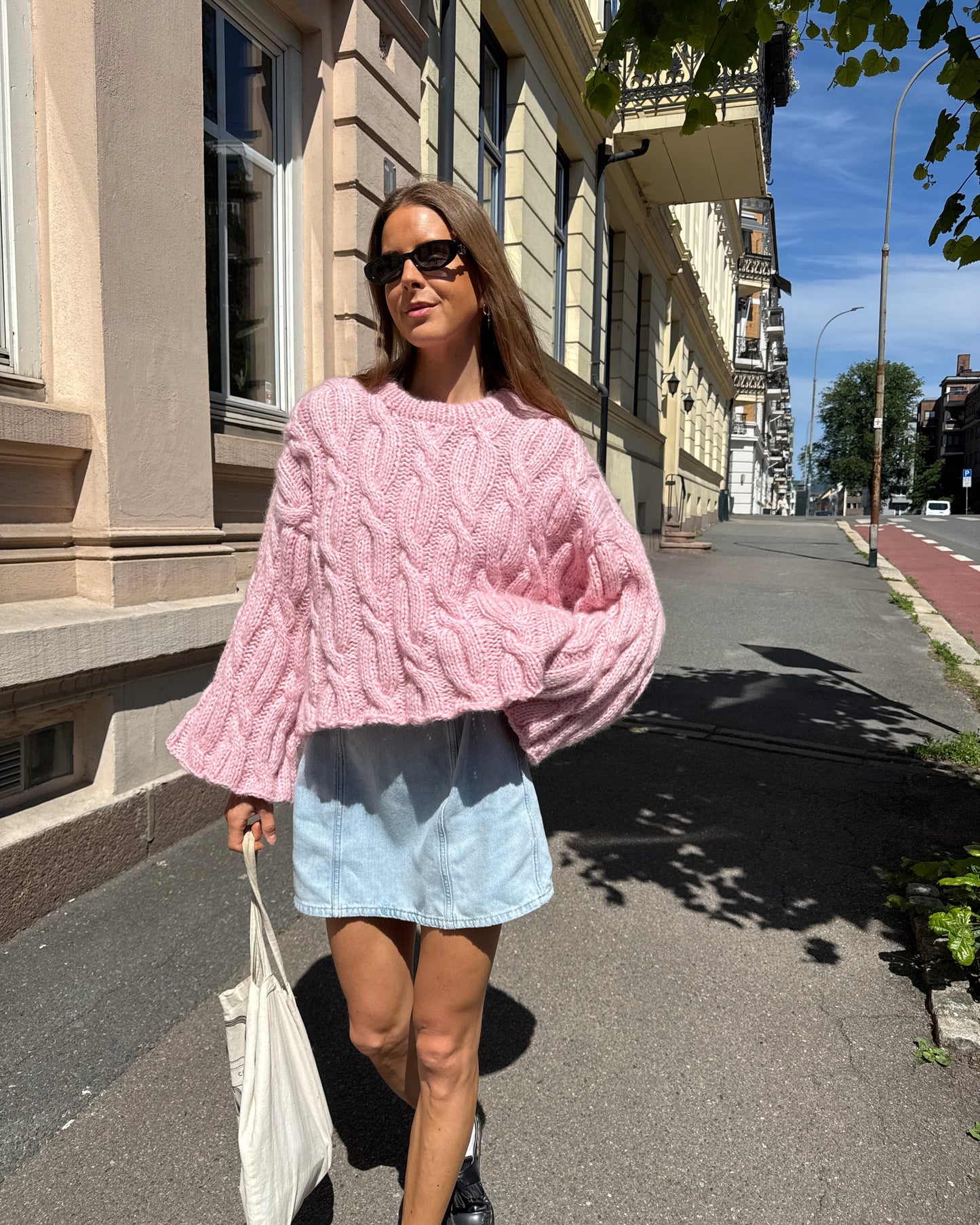 Person wearing a pink textured sweater and light blue shirt on a street.