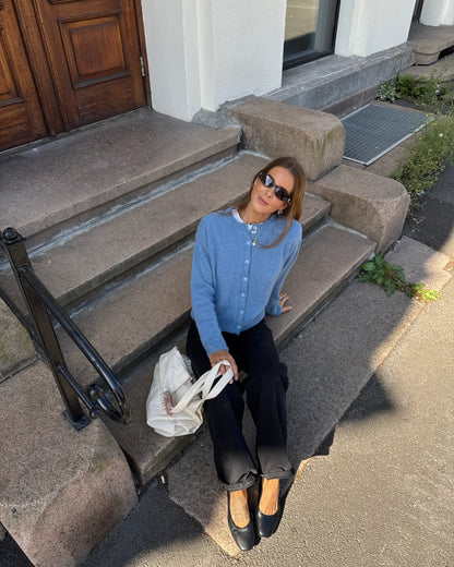 Person sitting on a stone bench with a handbag, wearing sunglasses and a blue jacket.